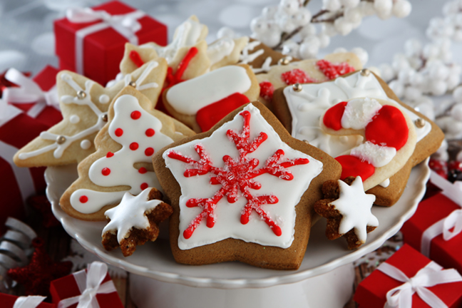 A round white platter displays a variety of decorated Christmas cookies, including trees, snowflakes, and stockings, with red and white icing and festive designs.