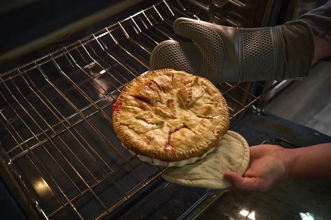 Hands removing a baked pie from the over