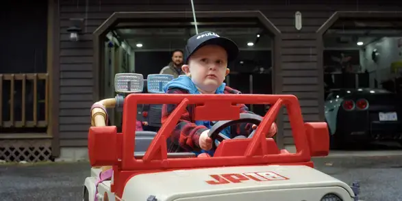 Patient Connor Ponce posing in a toy car in front of his family