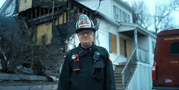 Patient Peter Lennon standing in front of a fire-damaged building