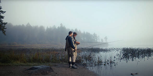 Two men engaged in fly fishing on the edge of a foggy lake