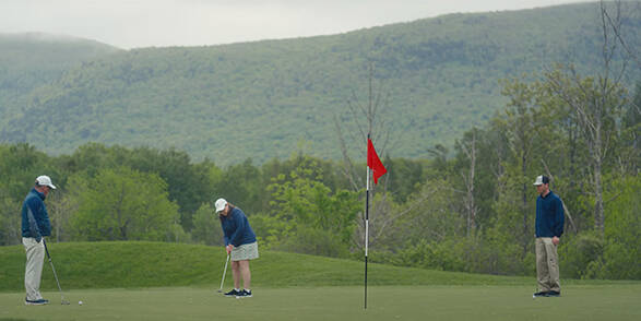 Two men and a woman playing golf with a lush mountainous backdrop