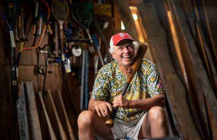 Bill Lee is shown sitting in his workshop holding a baseball bat he made.