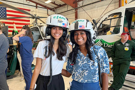 Two students wearing DHART helmets near a DHART helicopter