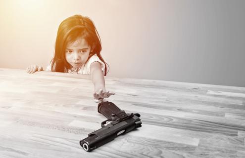 A child reaching across a table to a handgun