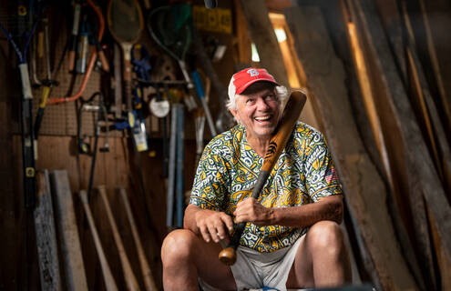 Bill Lee is shown sitting in his workshop holding a baseball bat he made.