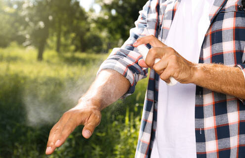 torso of a man outdoors spraying bug repellent on his arm