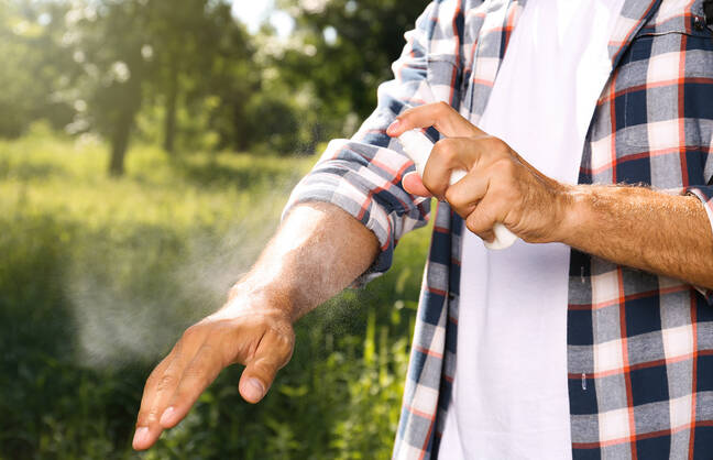 Man in a flannel shirt spraying insect repellant on his arm