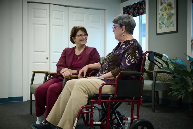 Nurse Susan Januszewski sits talking with a person in a wheelchair