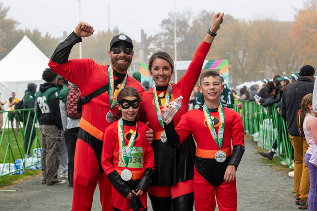 Triumphant, smiling family of four dressed in Incredibles costumes at the CHaD Hero